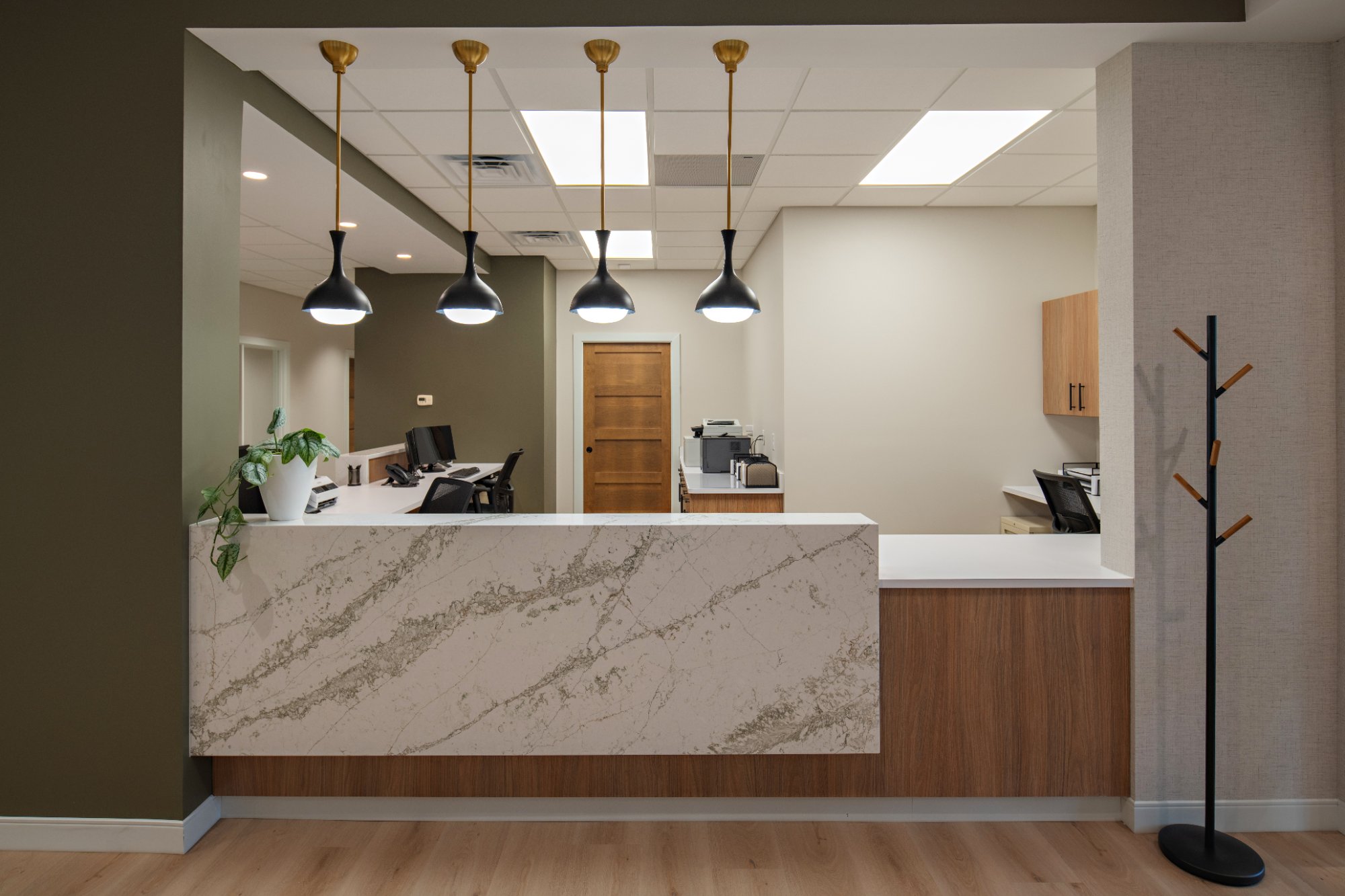 Dental-office-reception-desk-with-white-stone-front-panel-wood-veneer-cabinetry-and-black-brass-pendant-lights