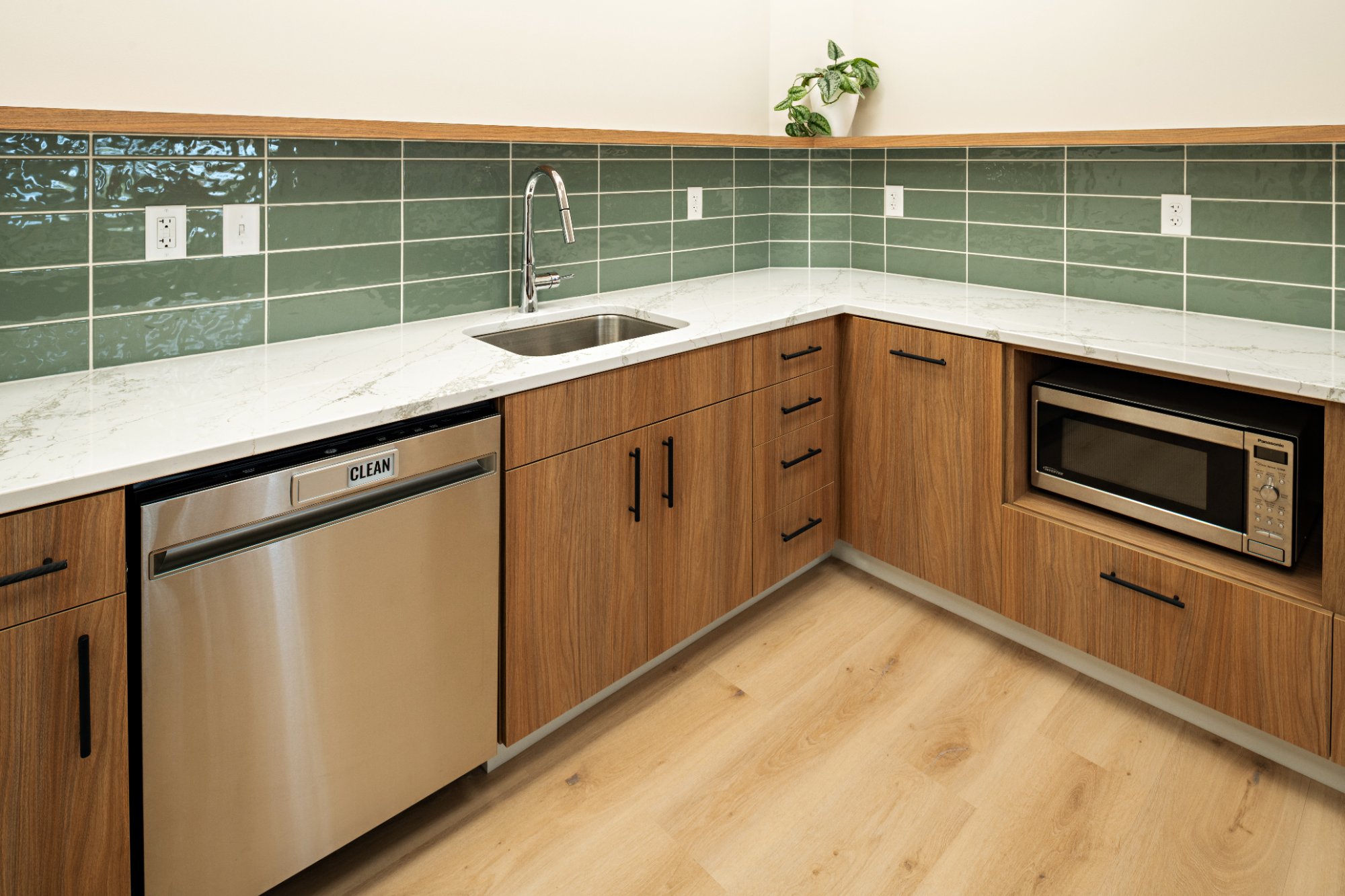 Dental office staff kitchen with walnut cabinetry quartz countertops sage green tile backsplash dishwasher and microwave