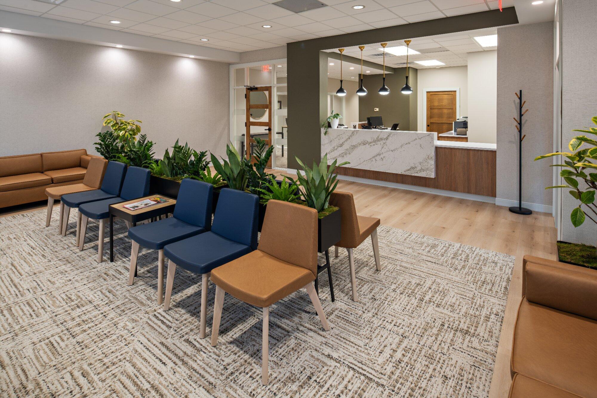Dental-office-waiting-area-opposite-angle-with-navy-tan-chairs-indoor-plants-leather-sofa-and-stone-reception-desk