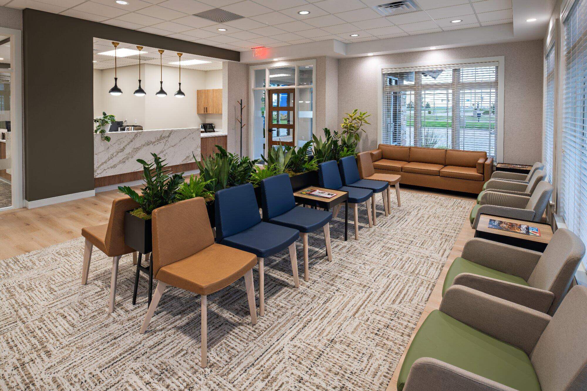 Dental office waiting&nbsp;room with tan navy and sage green seating indoor plants reception desk and pendant lights