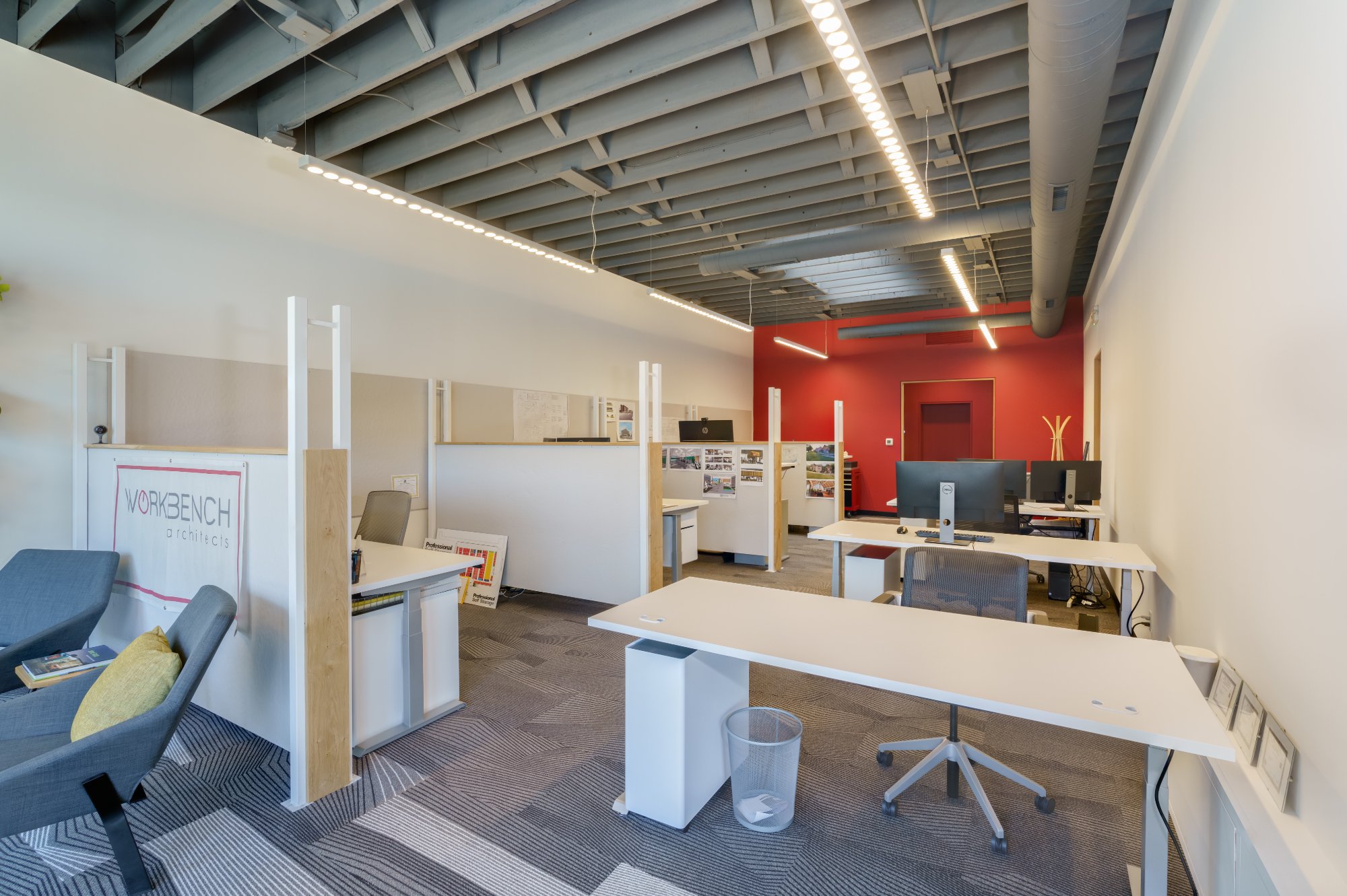 open plan office interior with white workstations red accent wall and exposed steel ceiling