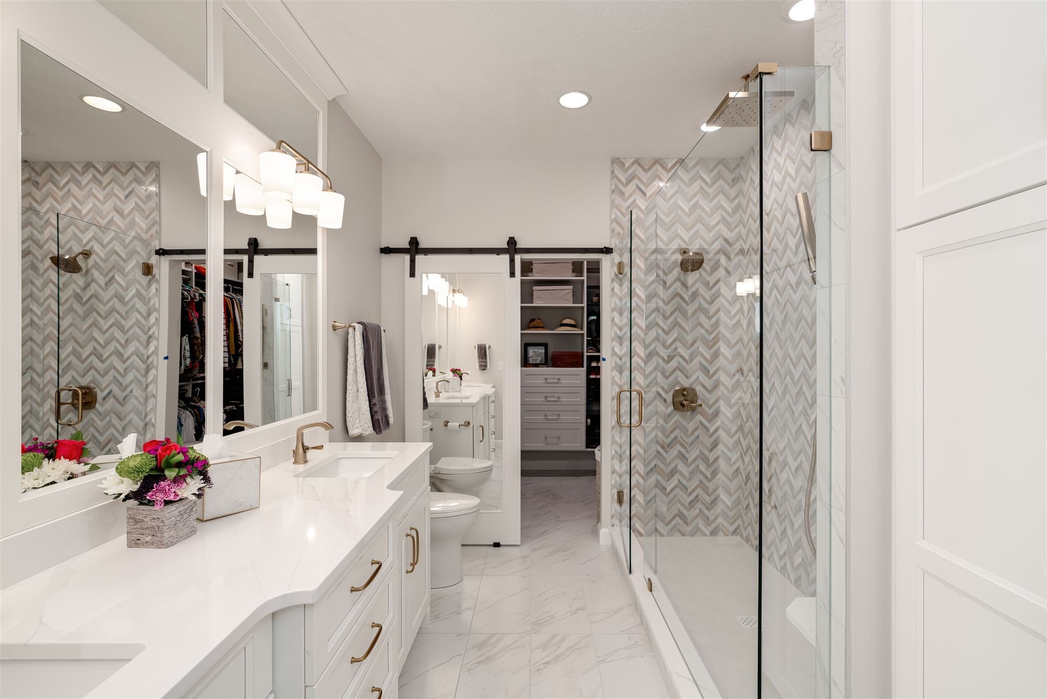 Bright bathroom in Bloomington, IL featuring double vanity, glass shower and entry to a walk-in closet
