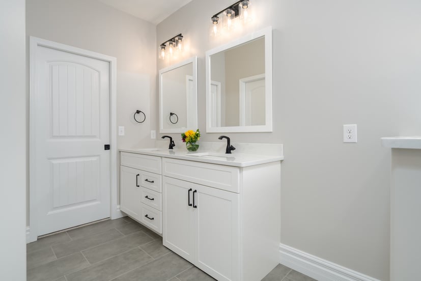 Bright bathroom in Bloomington, IL with white double vanity, black fixtures and gray tile flooring