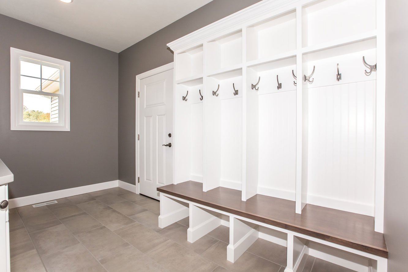 Bright mudroom with white built-in cubbies, wood bench, and tile flooring located in Illinois, built by Landmark Construction