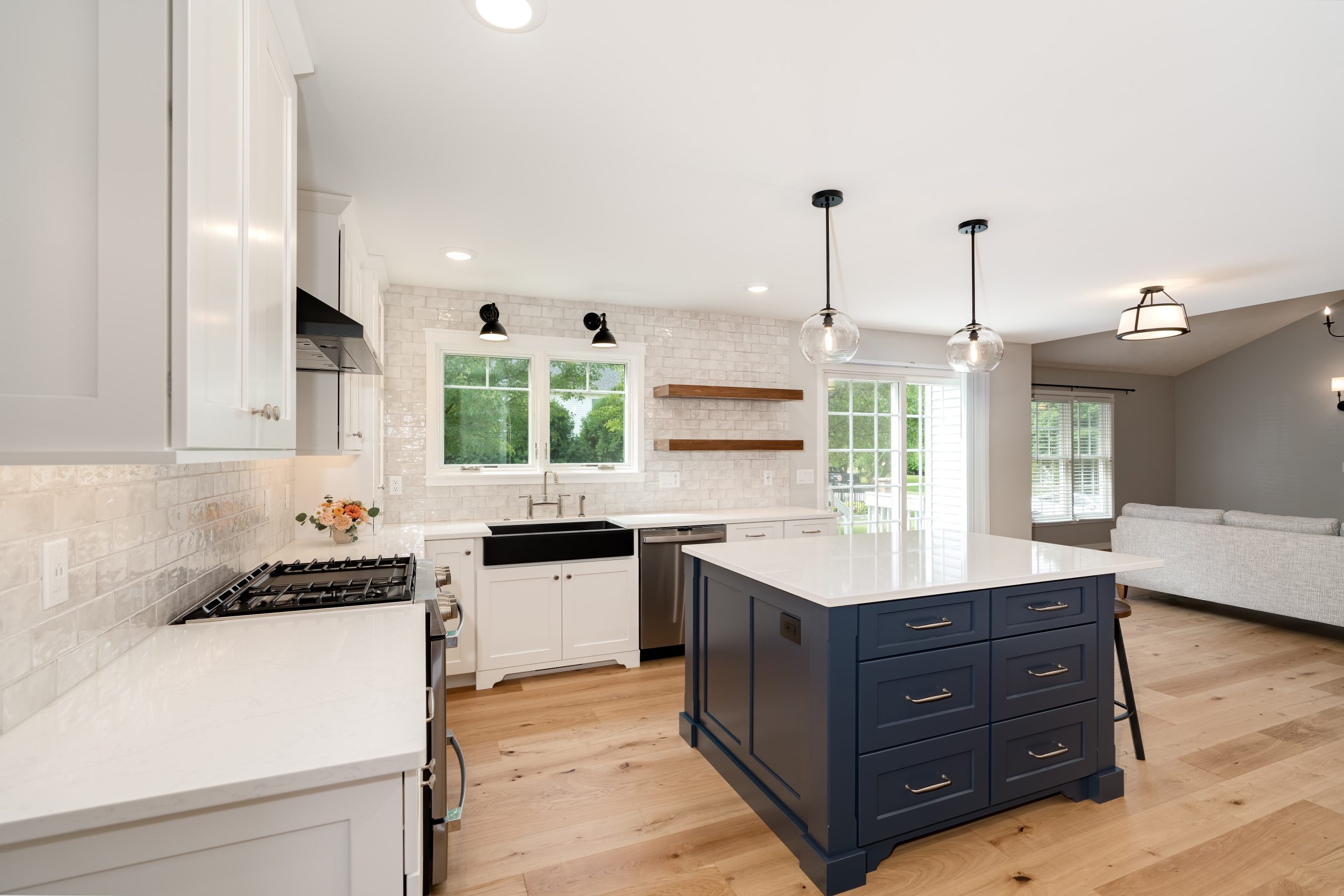 Bright white kitchen with a navy island, wood floors and modern lighting located in Bloomington, IL, built by Landmark Construction