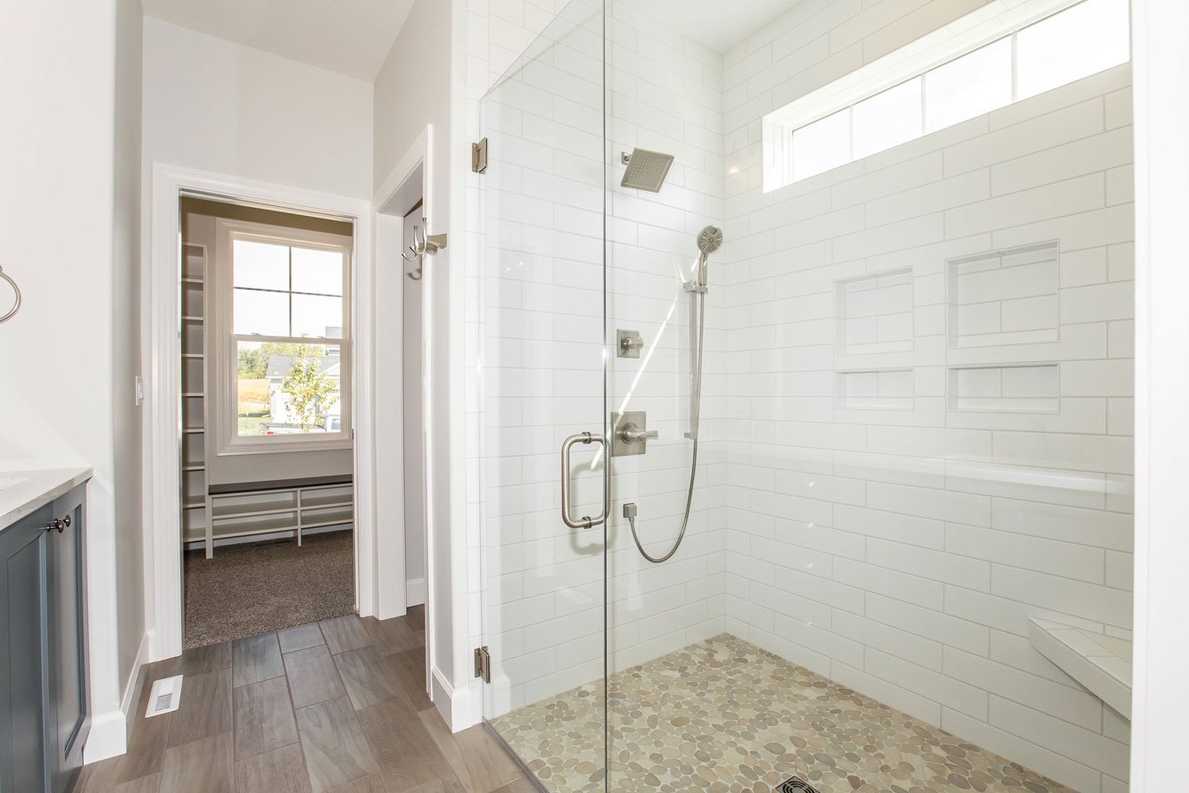 Glass walk in shower in Bloomington Normal with white subway tile, pebble floor, built in niches and bench