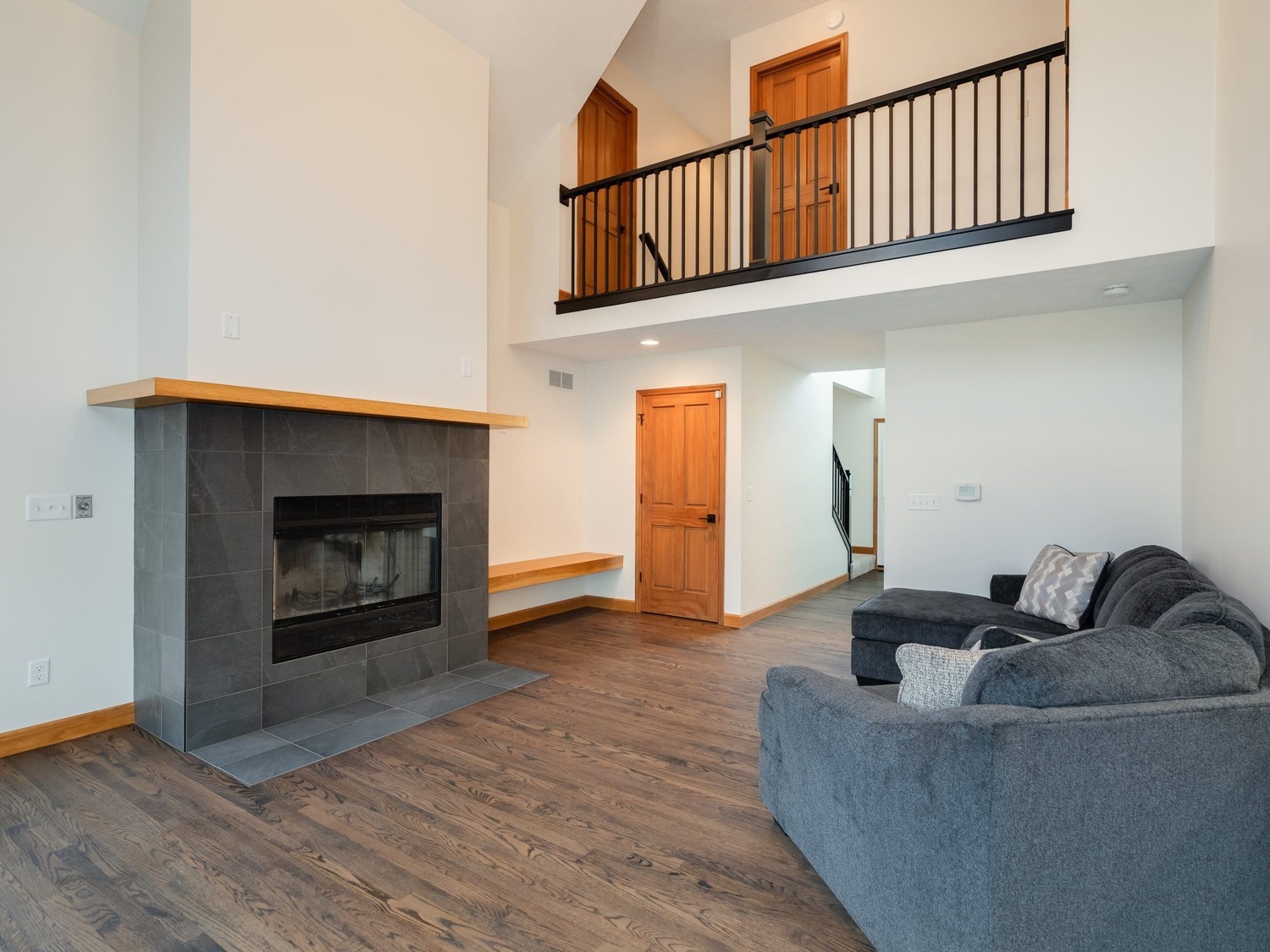 Living room in Bloomington Normal with dark tile fireplace, loft railing, wood floors and gray sectional