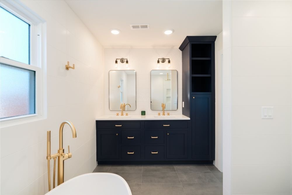 Modern bathroom with navy double vanity, brass fixtures, and freestanding tub built by Landmark Construction and located in Illinois