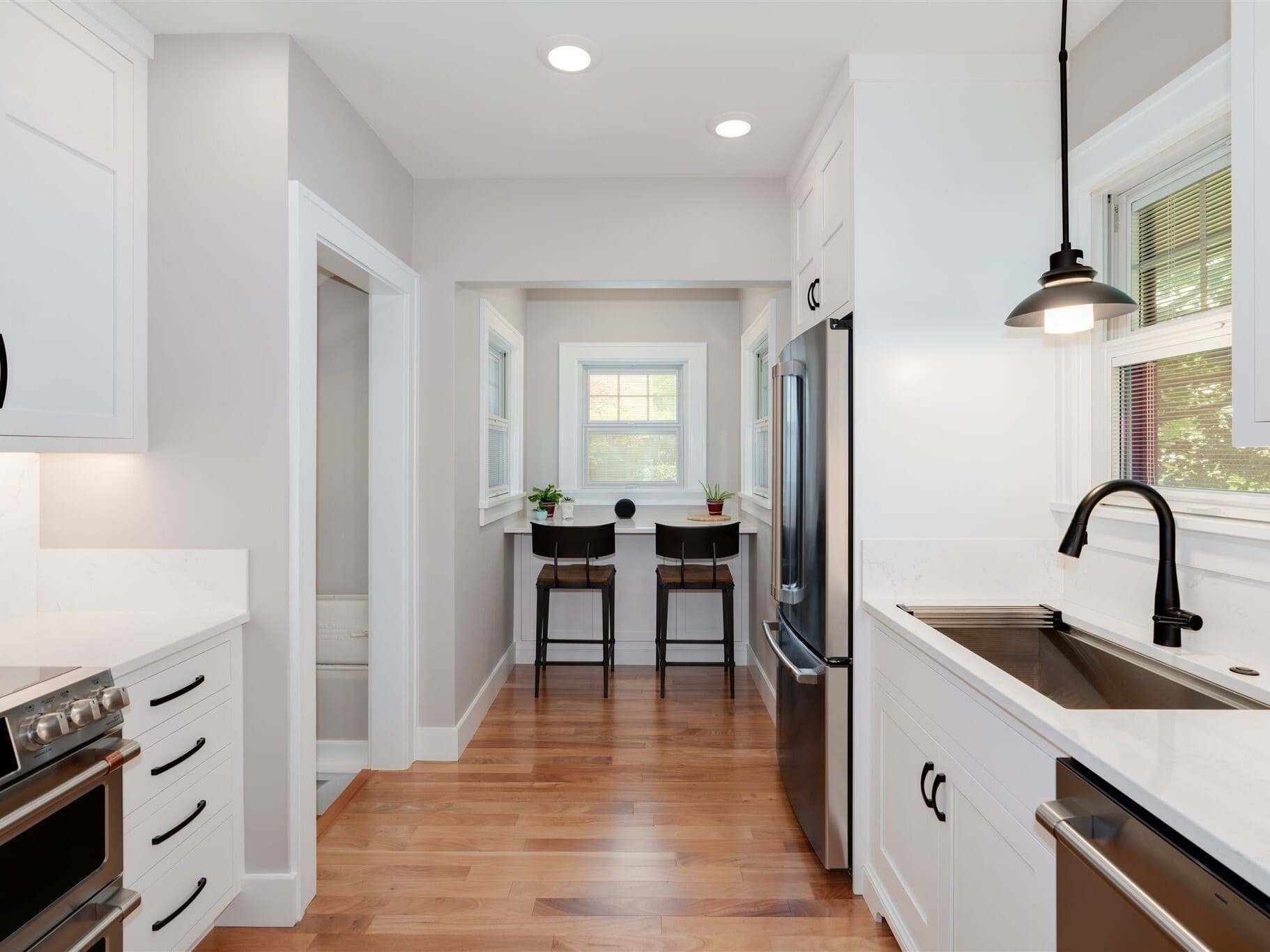 Narrow galley kitchen in Bloomington Normal with white cabinets, black faucet, stainless fridge and breakfast nook