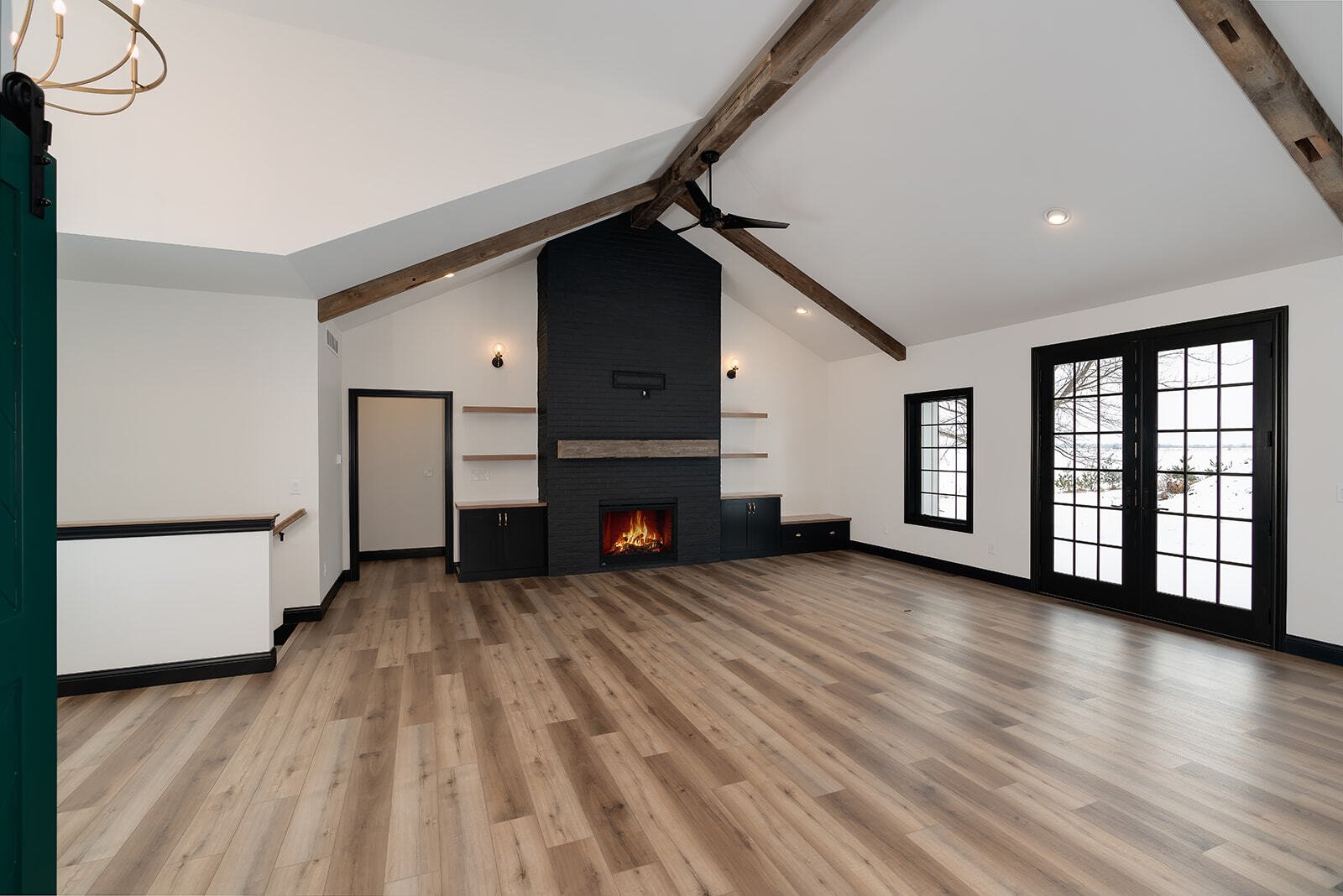 Spacious living room with vaulted ceilings, wood beams and a black fireplace wall, by Landmark Construction