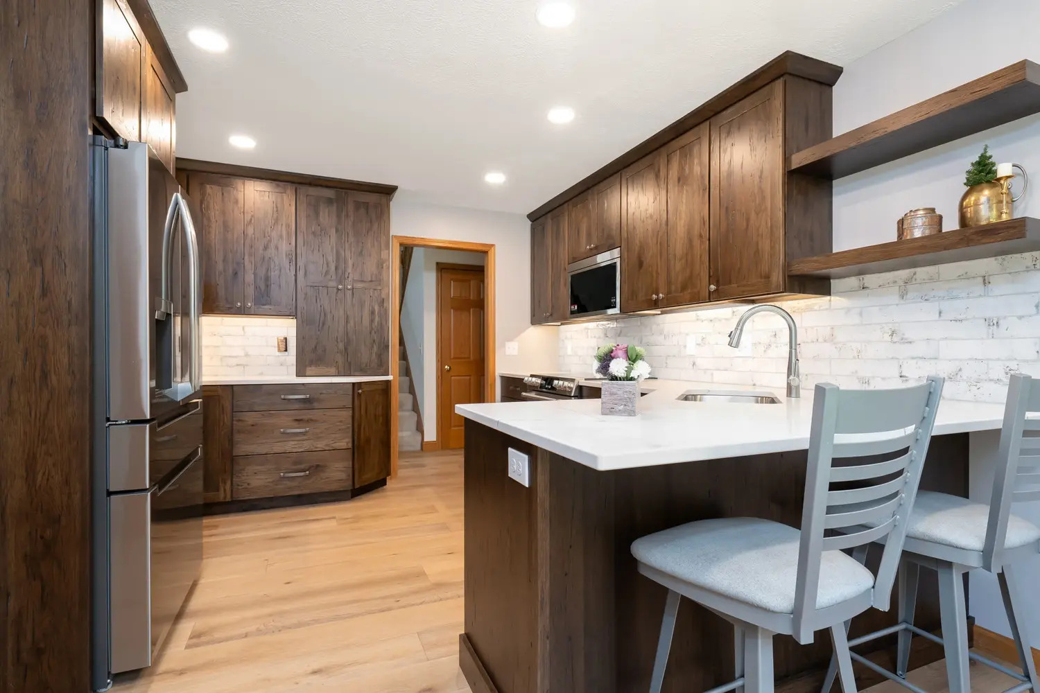 Modern kitchen with warm wood cabinets, white countertops, and breakfast bar seating located in Bloomington, IL, built by Landmark Construction