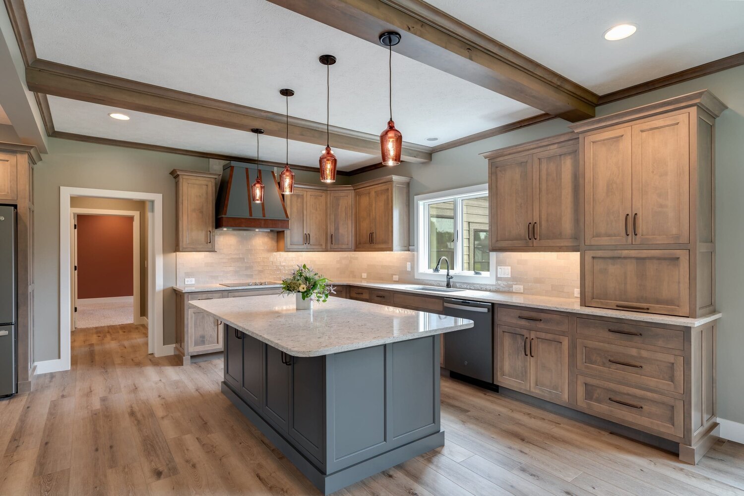 Rustic kitchen with wood cabinets, gray island, warm pendant lighting and stone countertops located in Bloomington, IL, built by Landmark Construction